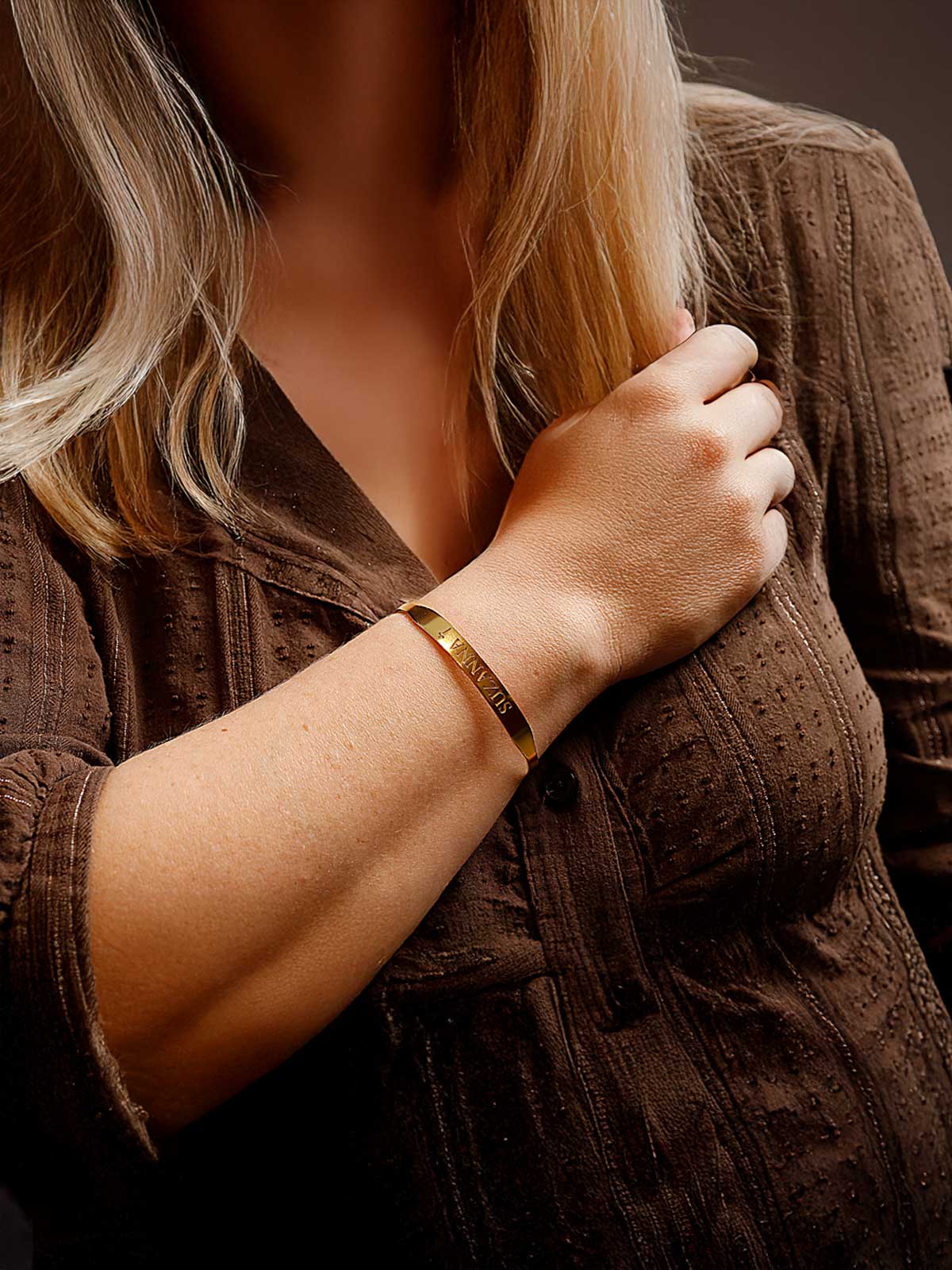 a woman wearing a gold bracelet and a brown shirt