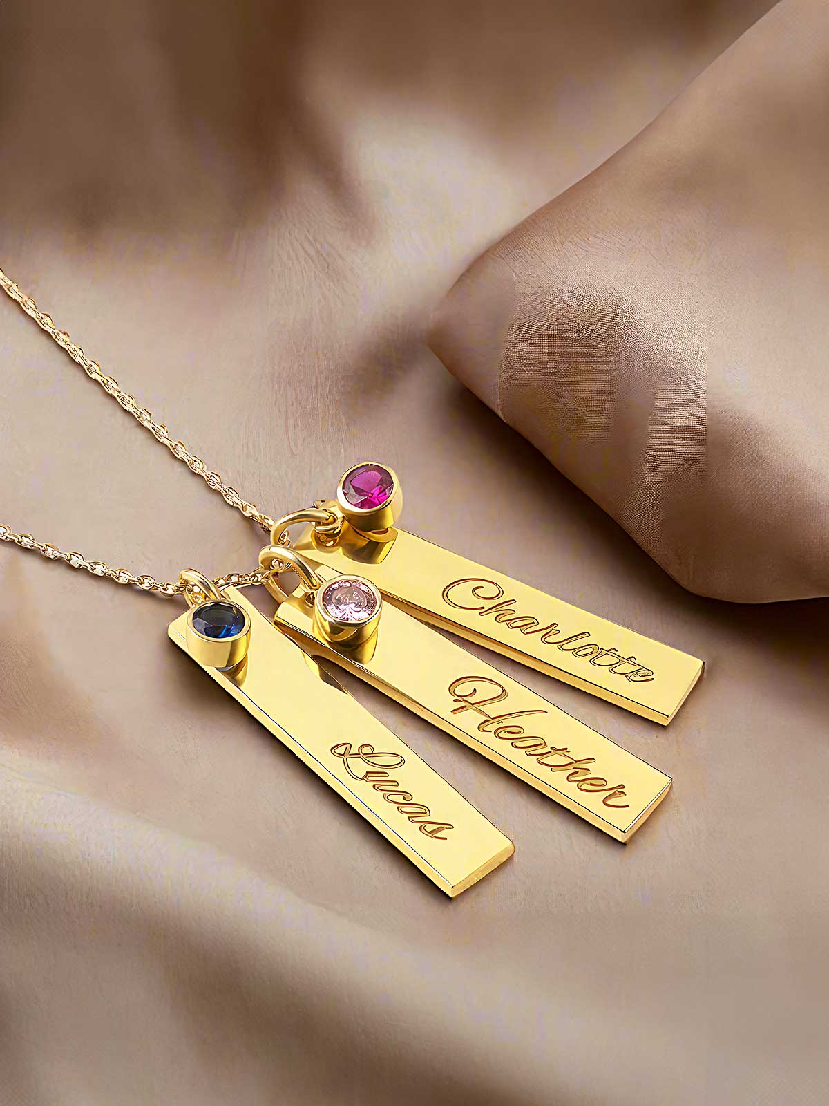 three personalized gold necklaces on a satin surface