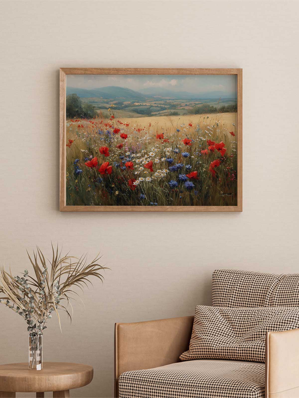 a framed painting of a field with red poppies and blue flowers hanging on a wall above a brown armchair with checkered pillows.