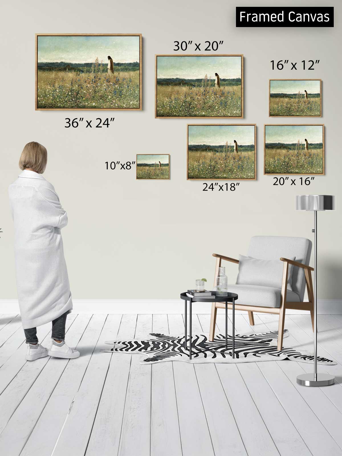 The image is a framed canvas display featuring a woman standing in a room with a zebra print rug, a white chair, and a table with a glass on it. The display includes various sizes of paintings of a giraffe in a field, with the largest painting being 36" x 24" and the smallest being 10" x 8".
