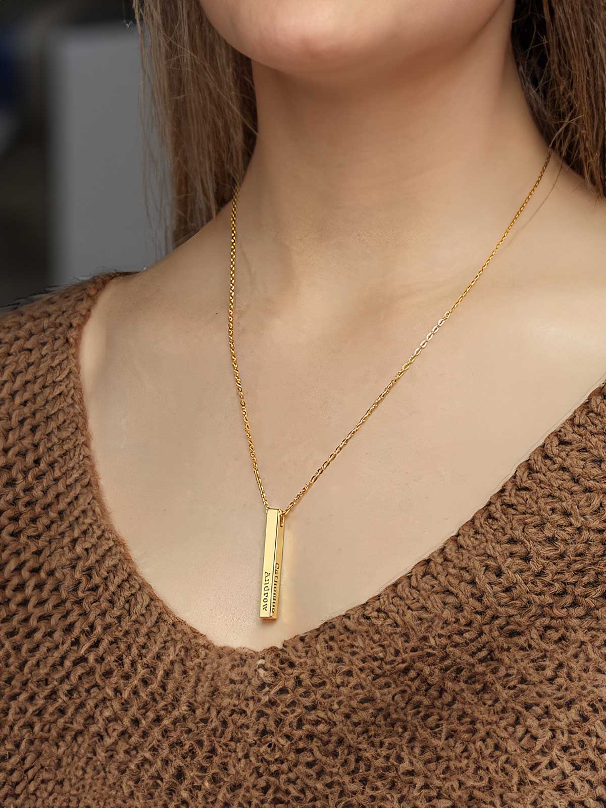 a woman wearing a gold necklace with a bar on it