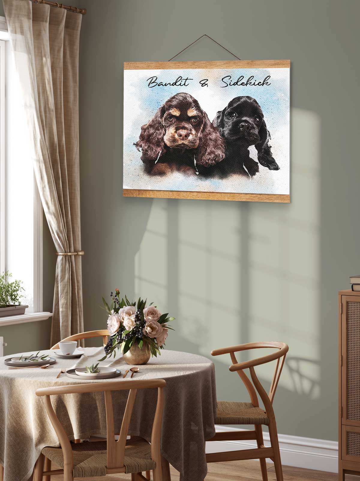 a framed painting of two dogs, one black and one brown, hanging on a wall above a wooden table with a vase of flowers.