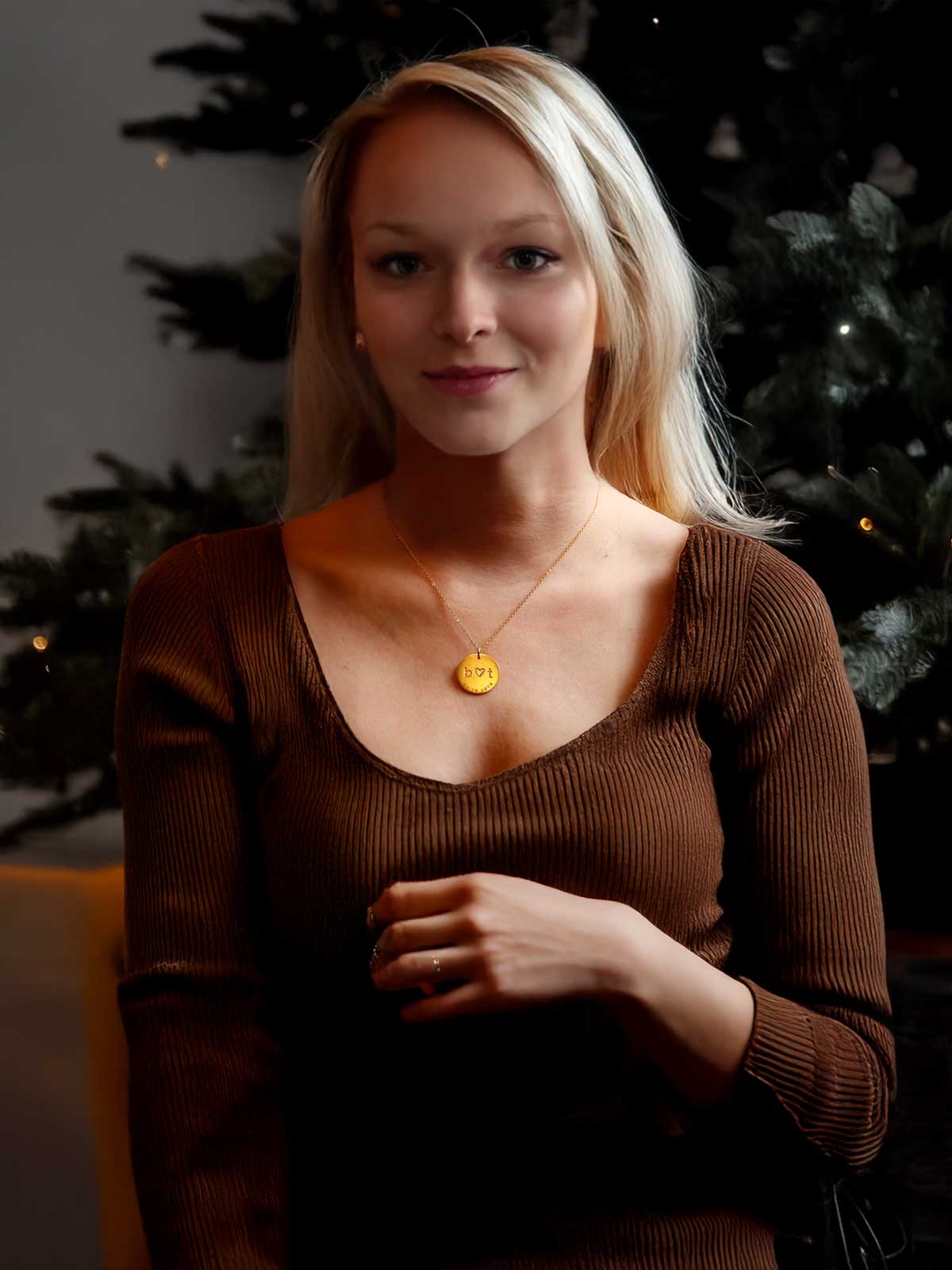 a woman in a brown sweater standing in front of a christmas tree