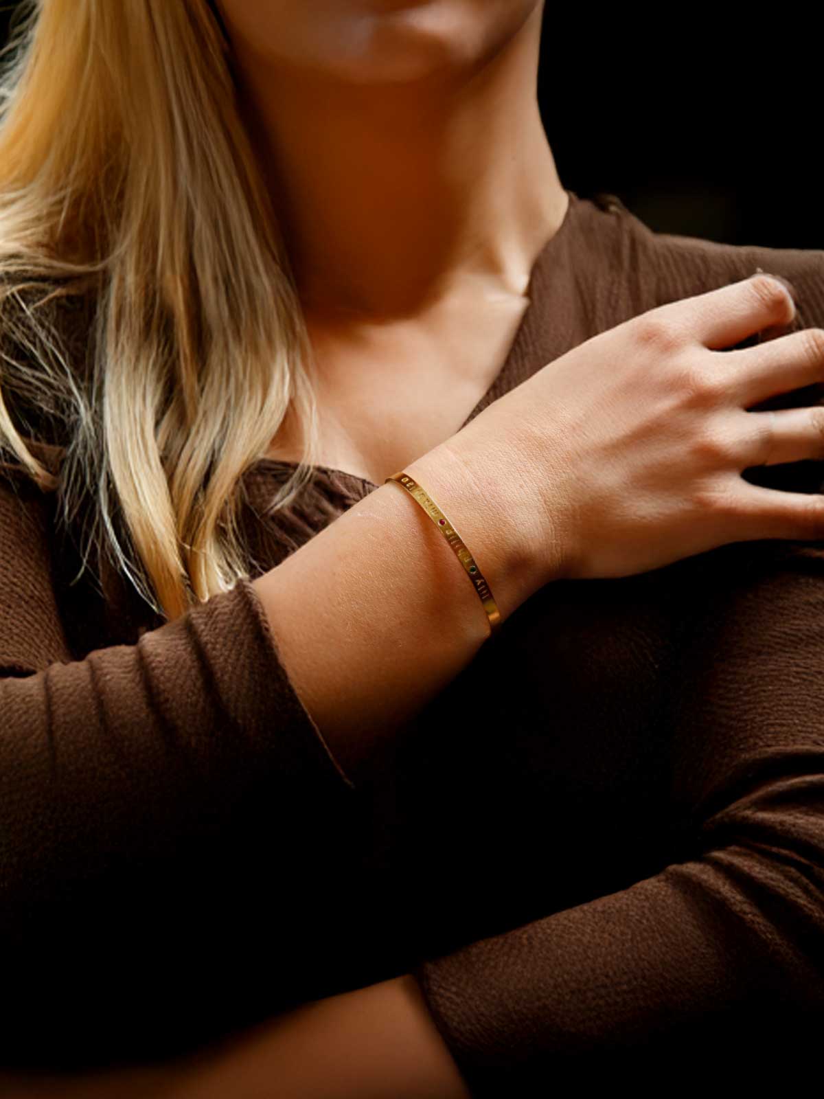 a woman wearing a gold bracelet and a brown shirt