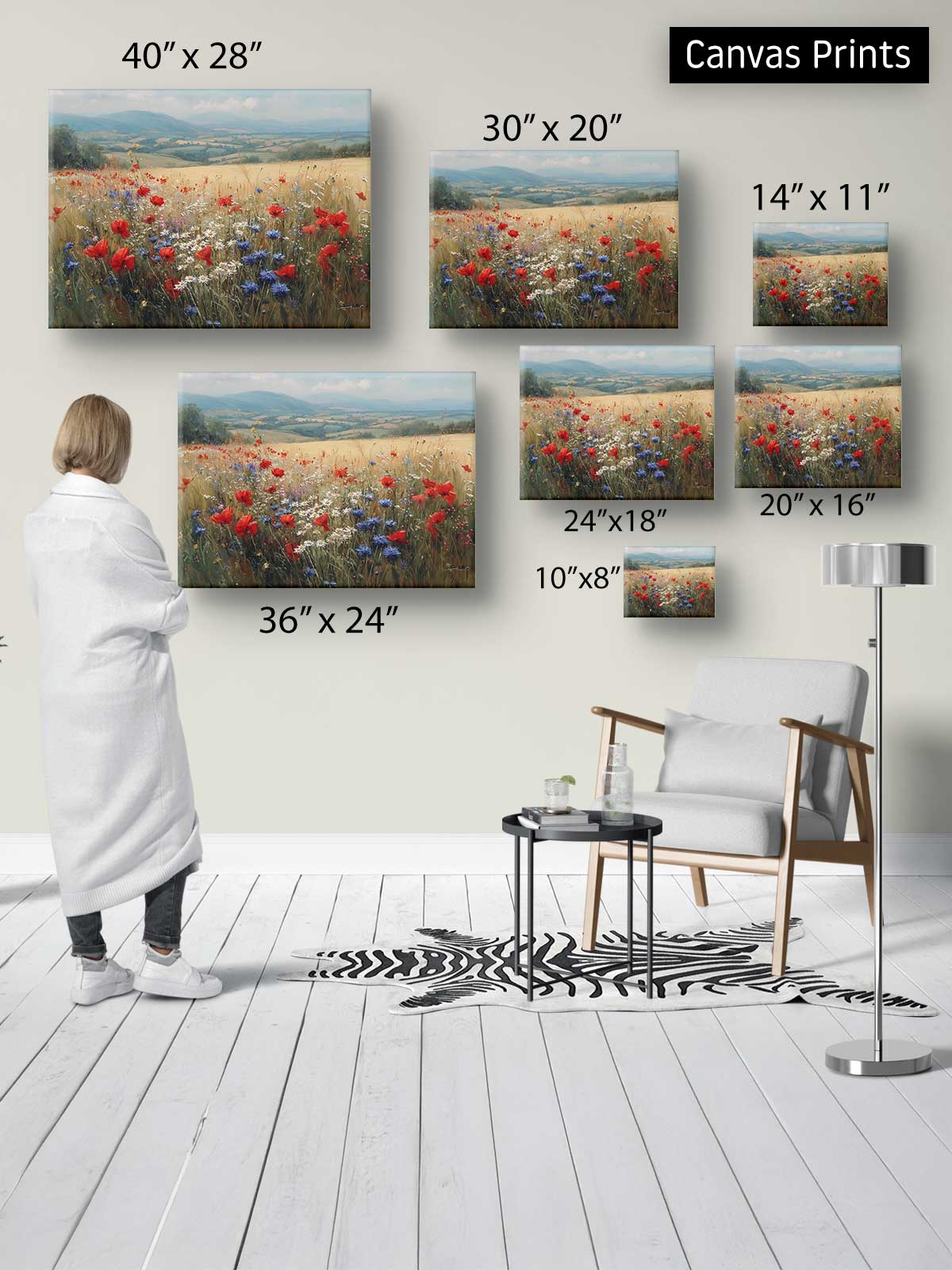 a person standing in a room, surrounded by various sizes of canvas prints depicting landscapes, including a field of flowers. The person appears to be examining the different canvas prints, which are displayed on the wall.