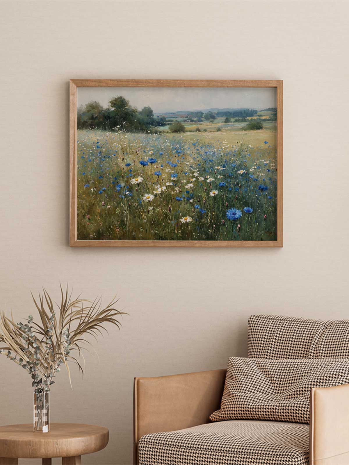 a framed painting of a field with blue and white flowers hanging on a wall above a brown armchair with checkered pillows.
