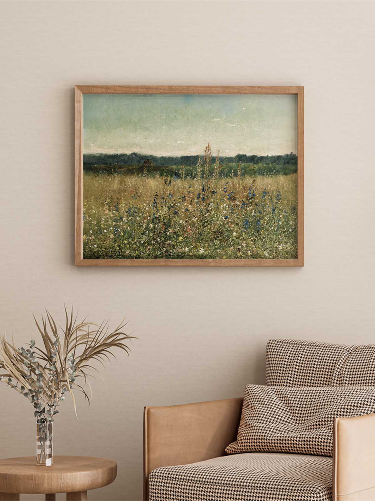 a painting of a field with tall grass and wildflowers hanging on a wall above a brown armchair with checkered pillows.